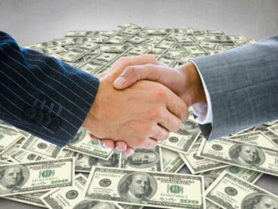Business people shaking hands against pile of dollars