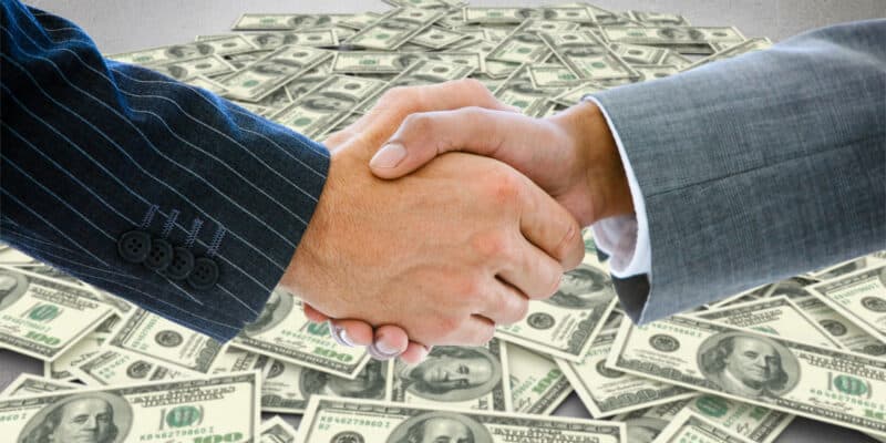 Business people shaking hands against pile of dollars
