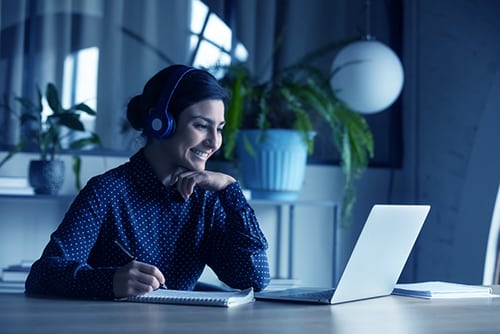 Happy young indian girl with wireless headphones looking at laptop screen